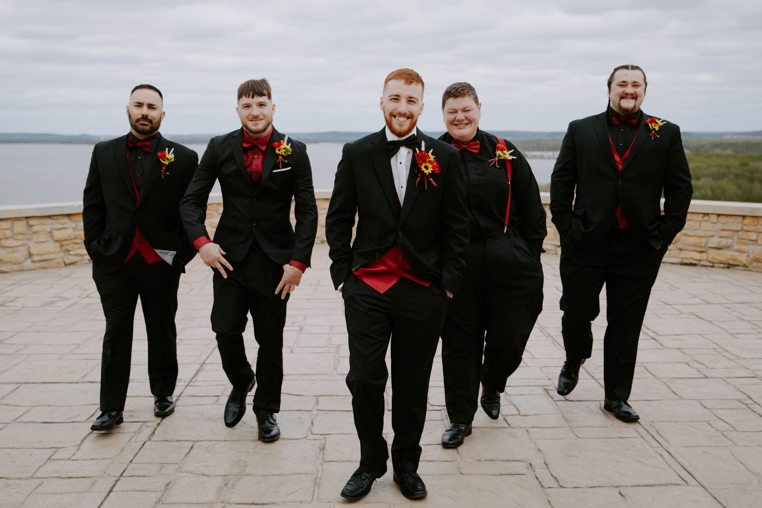 Groomsmen posing playfully in black suits against an overcast sky.