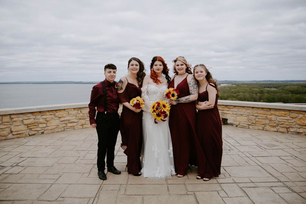 Wedding party in burgundy and black attire posing together on a stone patio.