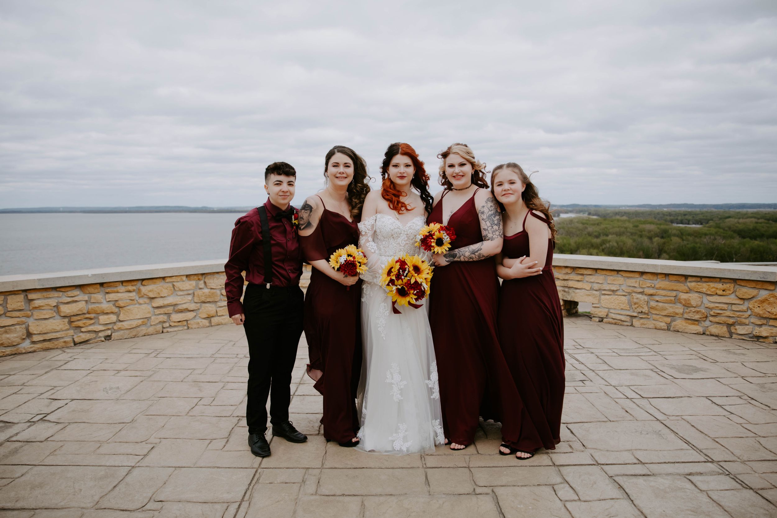 Wedding party in burgundy and black attire posing together on a stone patio.
