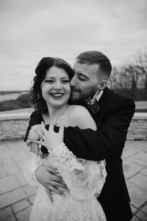Black and white wedding portrait captures tender moments between newlyweds on a stone terrace.