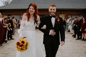Wedding celebration scene with couple walking past guests holding sunflower bouquet.