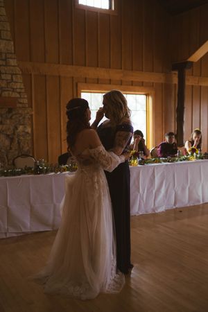 Silhouetted figures share a moment in a rustic wedding venue with white-clothed tables.