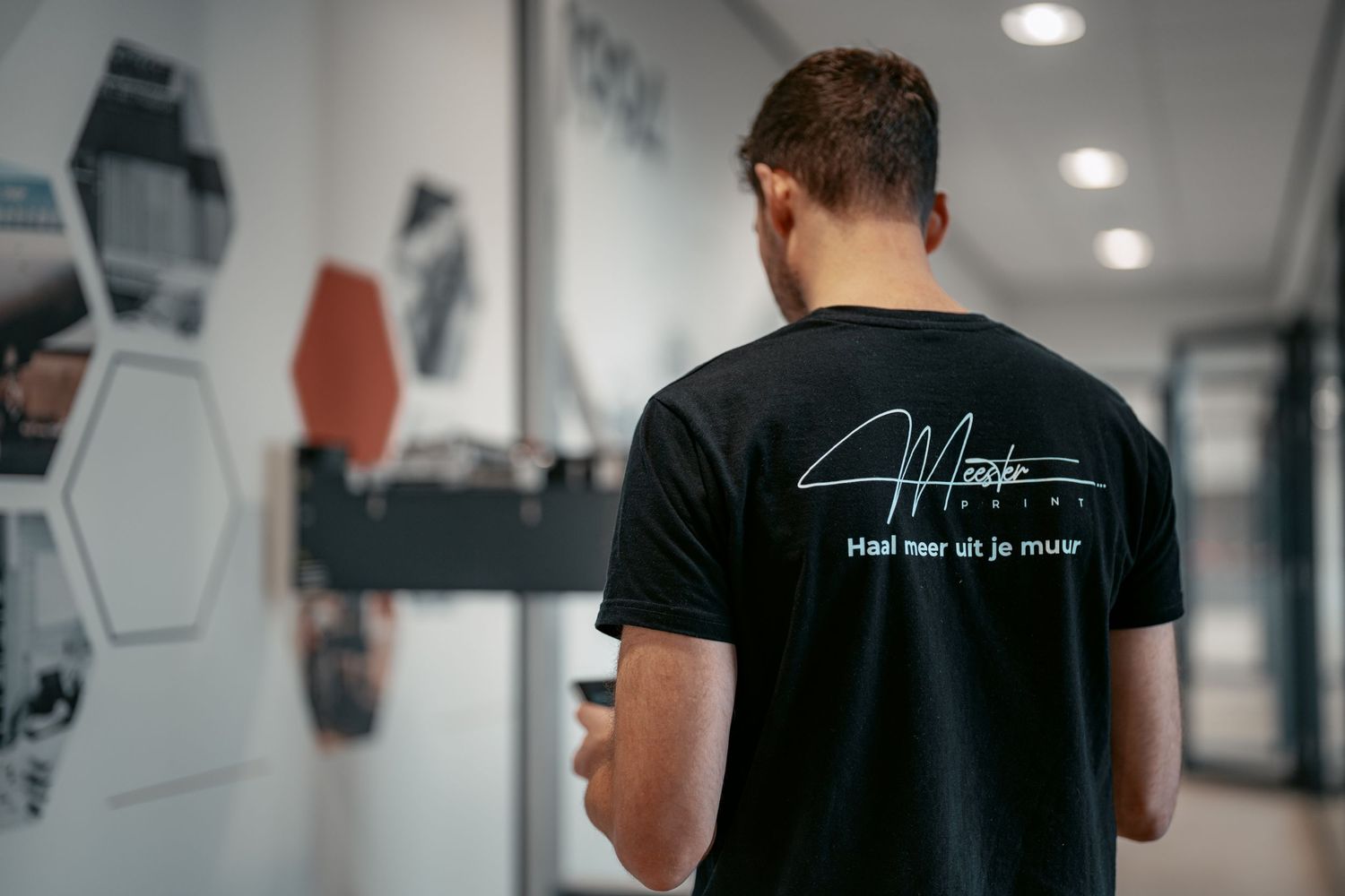 Back view of person wearing black t-shirt with signature design standing in modern office hallway.