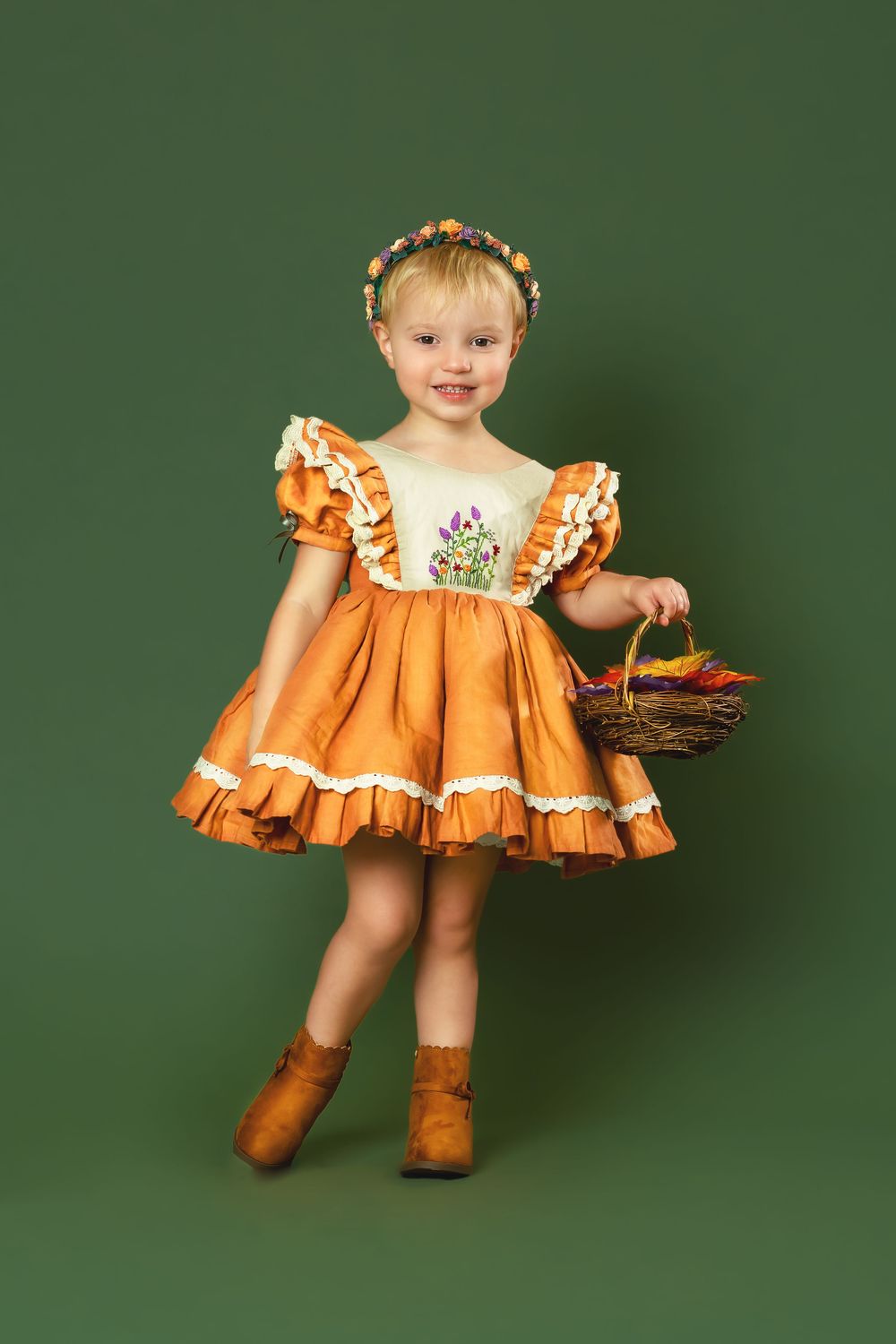 Orange ruffled dress photoshoot with rustic boots against green background.
