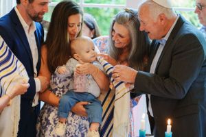 Multiple generations gather around a baby during what appears to be a religious ceremony or blessing with ritual elements.
