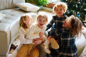 Group of young children playing and laughing together on a couch with a teddy bear during the holiday season.