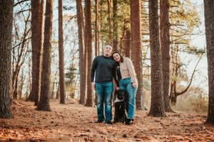 A couple and their dog walk together on a trail through a pine forest on an autumn afternoon.