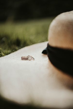 Wedding rings on the rim of a white sunhat sitting in grass with shallow depth of field.