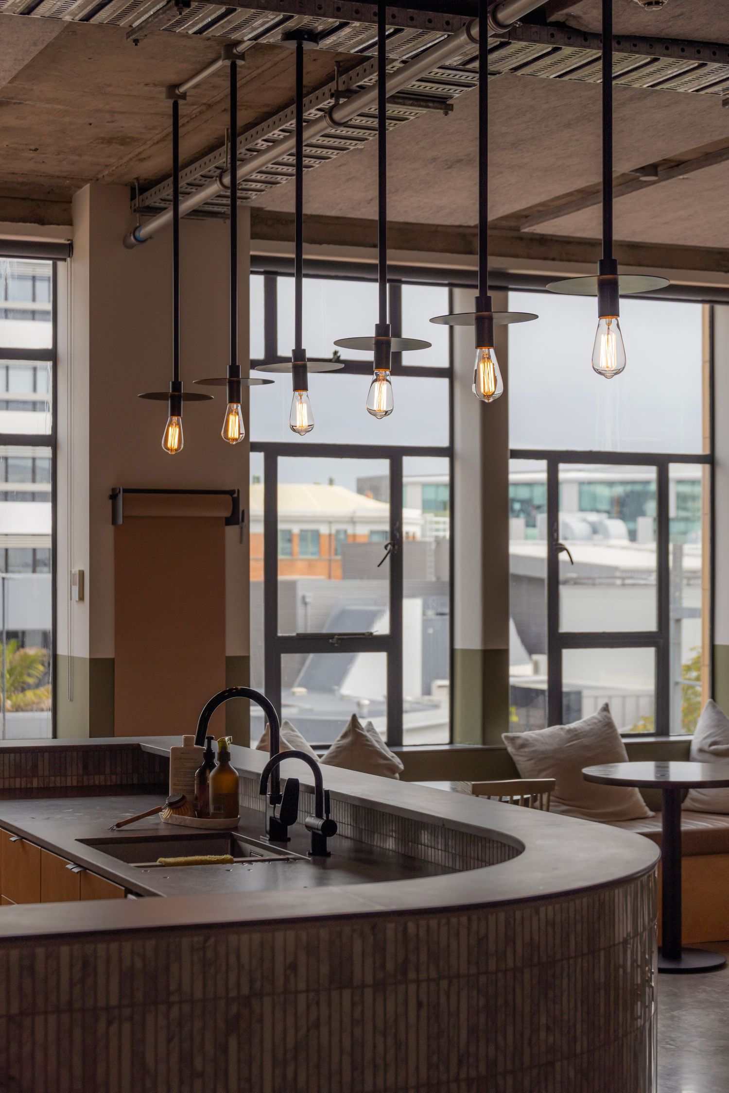 Open-plan kitchen with pendant lights, curved benchtops, and city views through floor-to-ceiling windows.