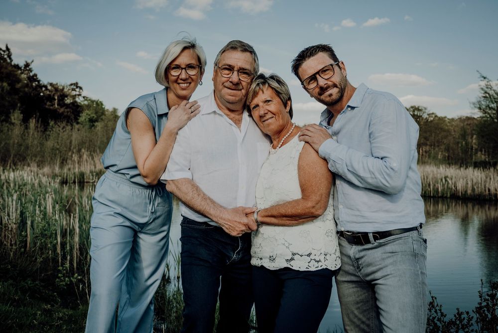 Four-generation family portrait with two older couples posing affectionately near a peaceful lakeside setting.