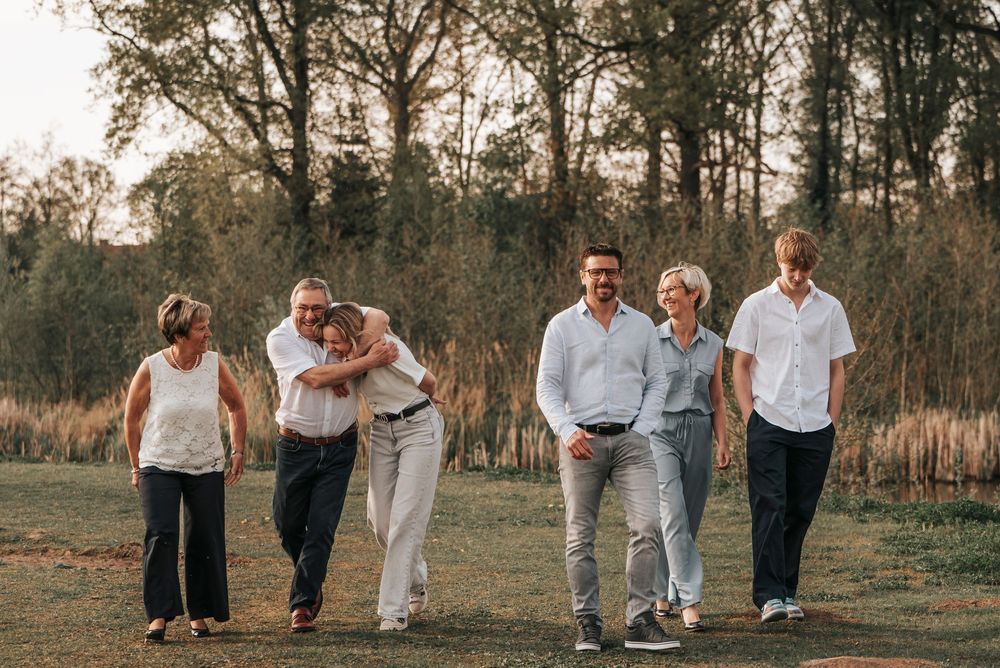 Extended family of six walking together through a sunlit park, sharing hugs and laughter at golden hour.