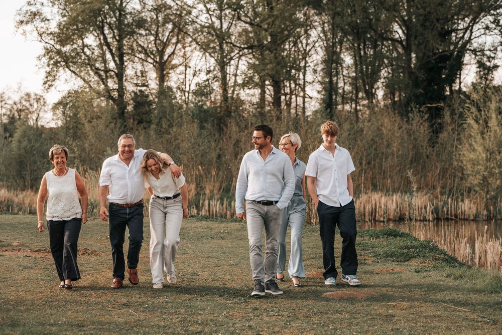 Six family members strolling casually through a scenic park with trees and a pond in warm evening light.