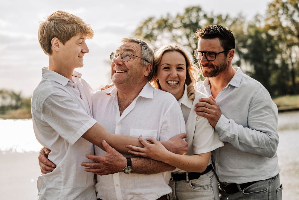 Happy multigenerational family laughing together outdoors near a lake during a warm summer day.