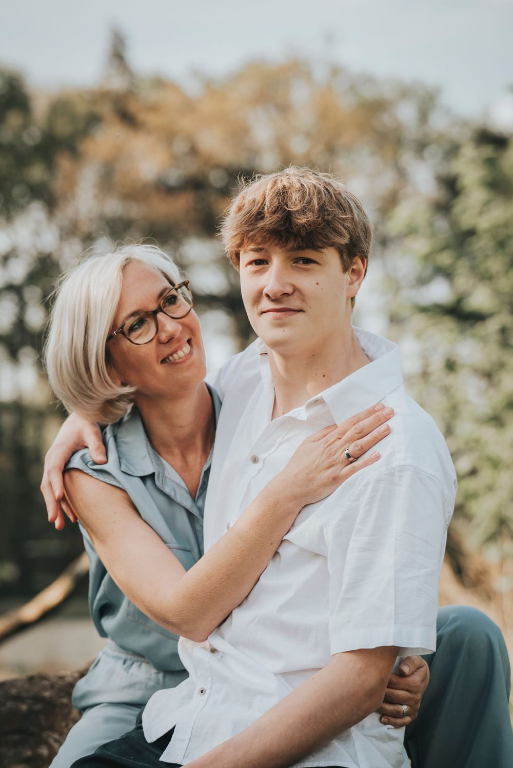 Smiling older woman with glasses embracing teenage son outdoors in a loving portrait.