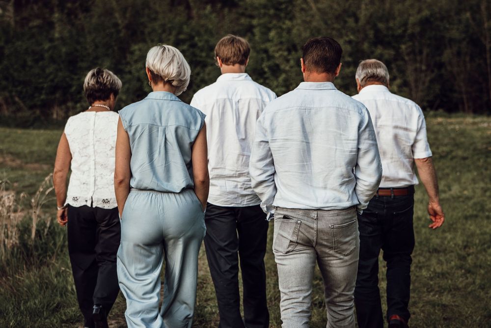 Back view of five family members walking together through a lush green meadow.