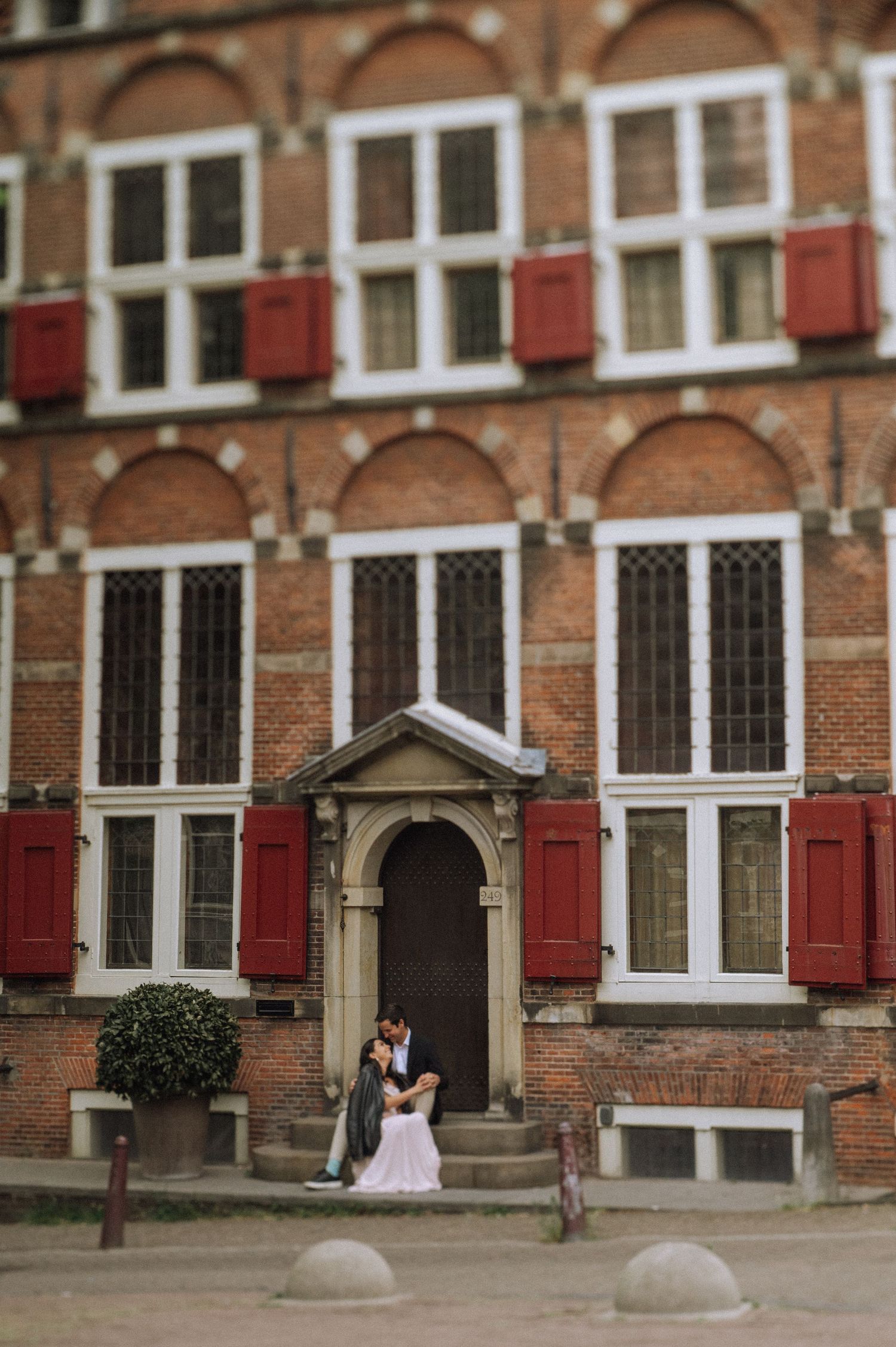 Casual lifestyle photo of a pregnant couple sitting on the steps of a historic Amsterdam townhouse