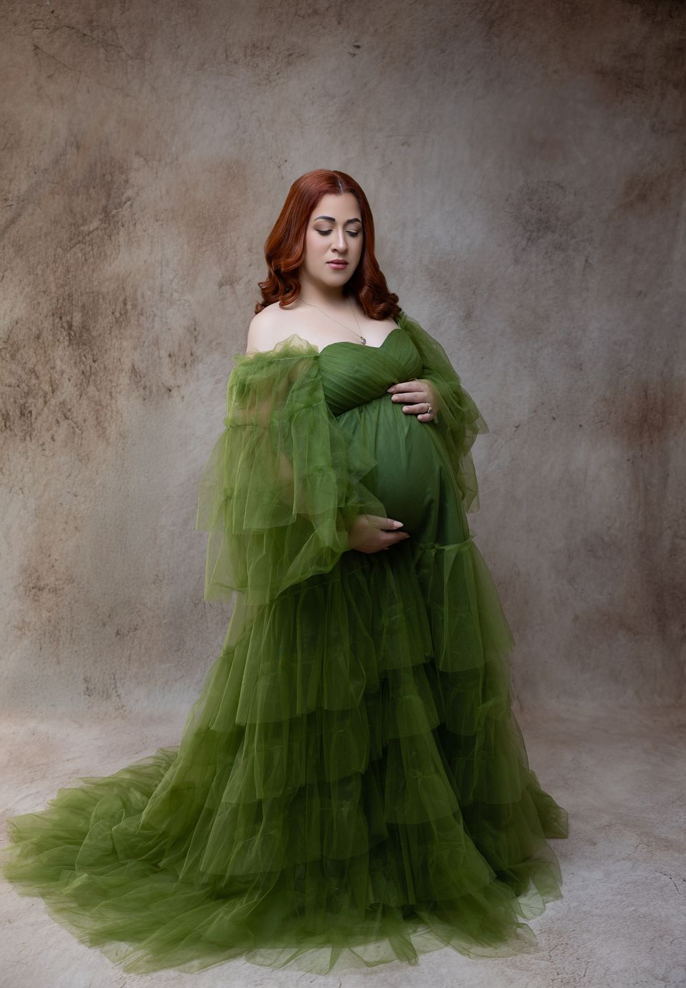 A figure in a flowing olive green tulle gown poses gracefully against a textured gray backdrop in a photo series.