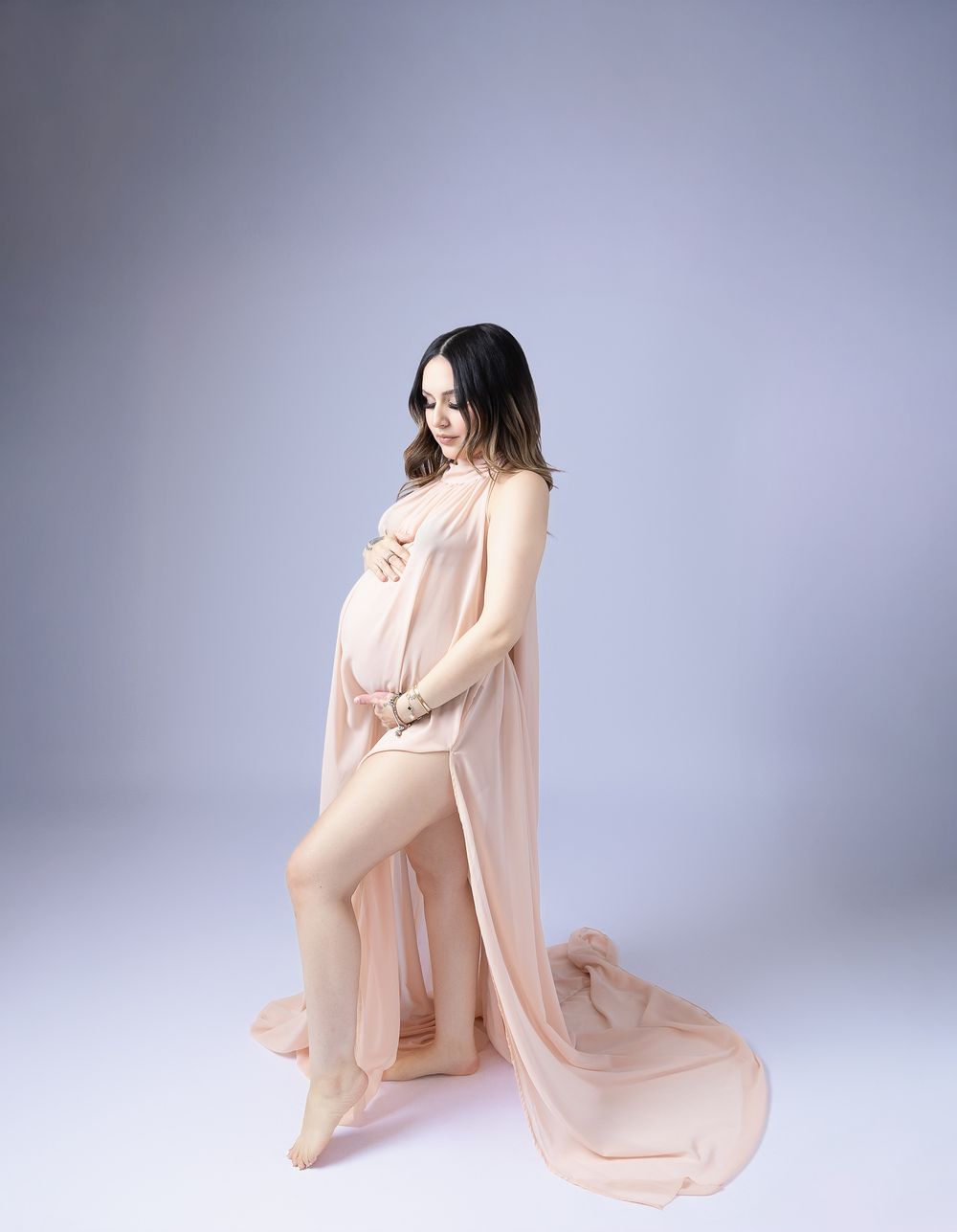 Artistic maternity portraits in flowing peach fabric against purple studio backdrop.