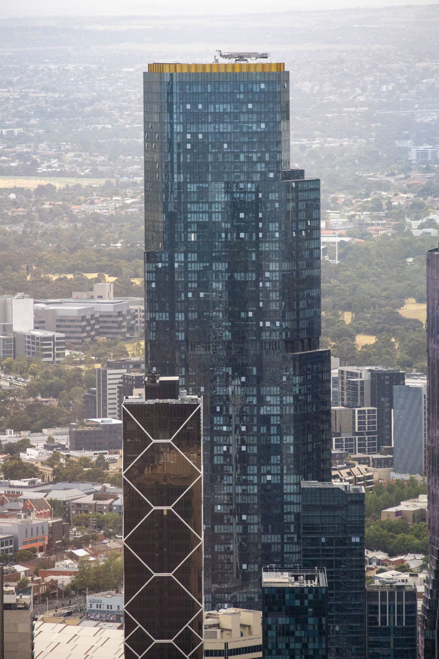Skyscraper with geometric facade detail rising above Melbourne’s urban skyline on a cloudy day.