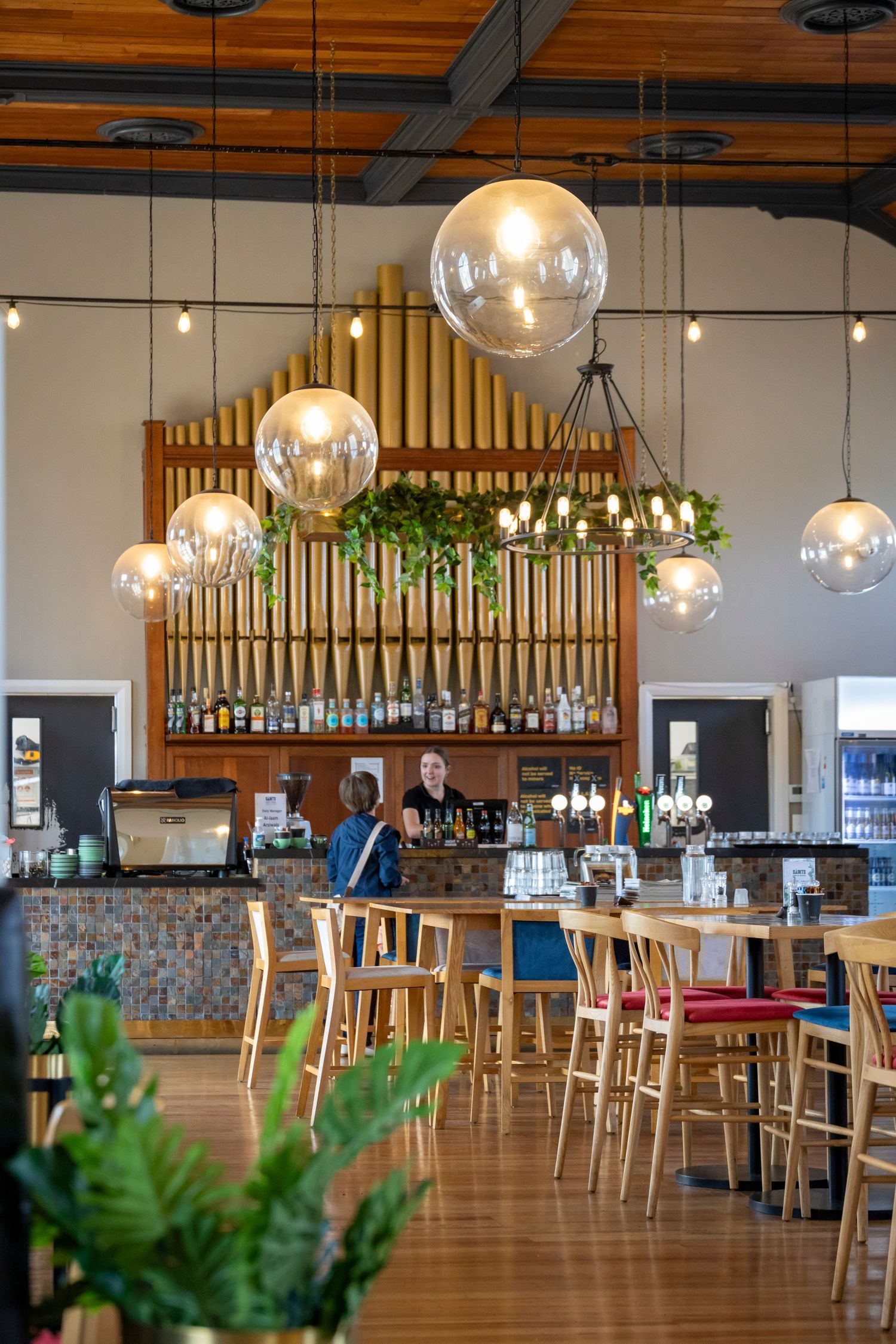 Stylish café interior with glowing globe lights, wooden bar and plants.
