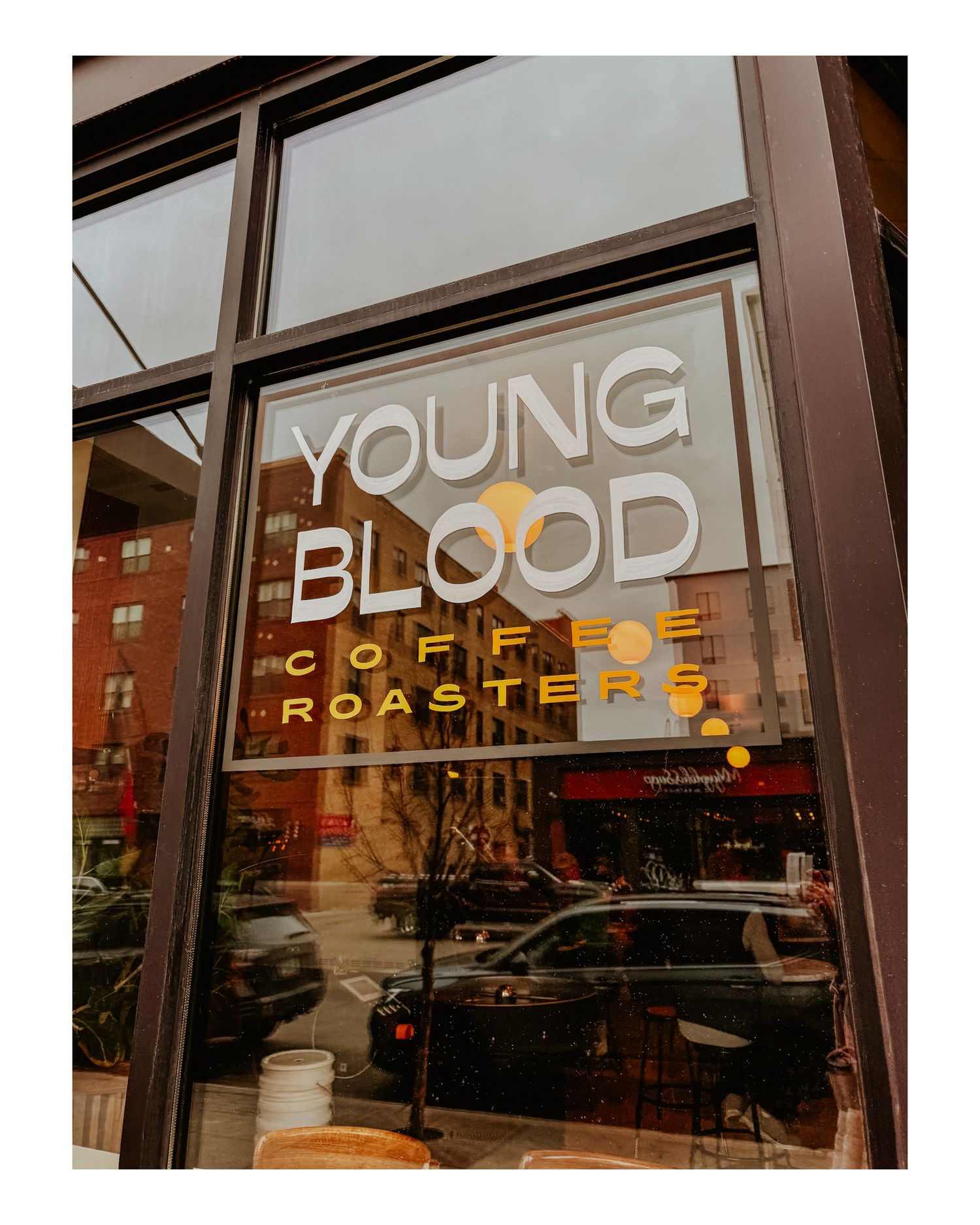 Young Blood Coffee Roasters storefront window sign with reflection of urban street scene.