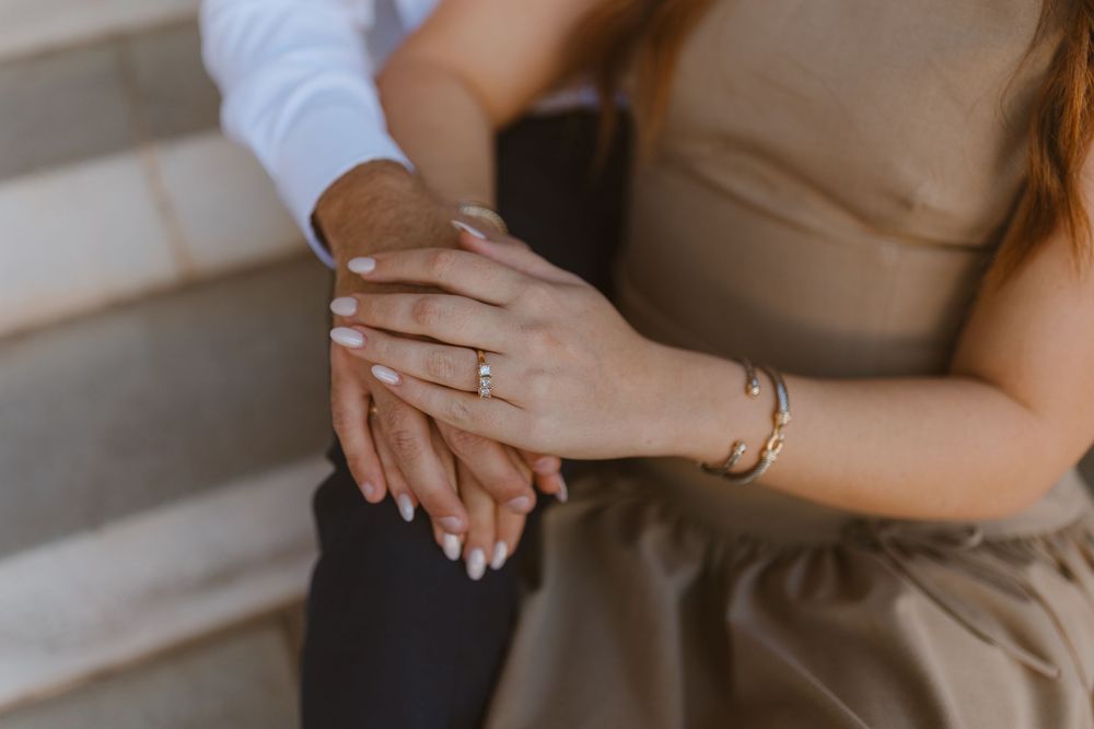 Close-up view of hands with wedding rings touching each other against a backdrop of beige clothing.