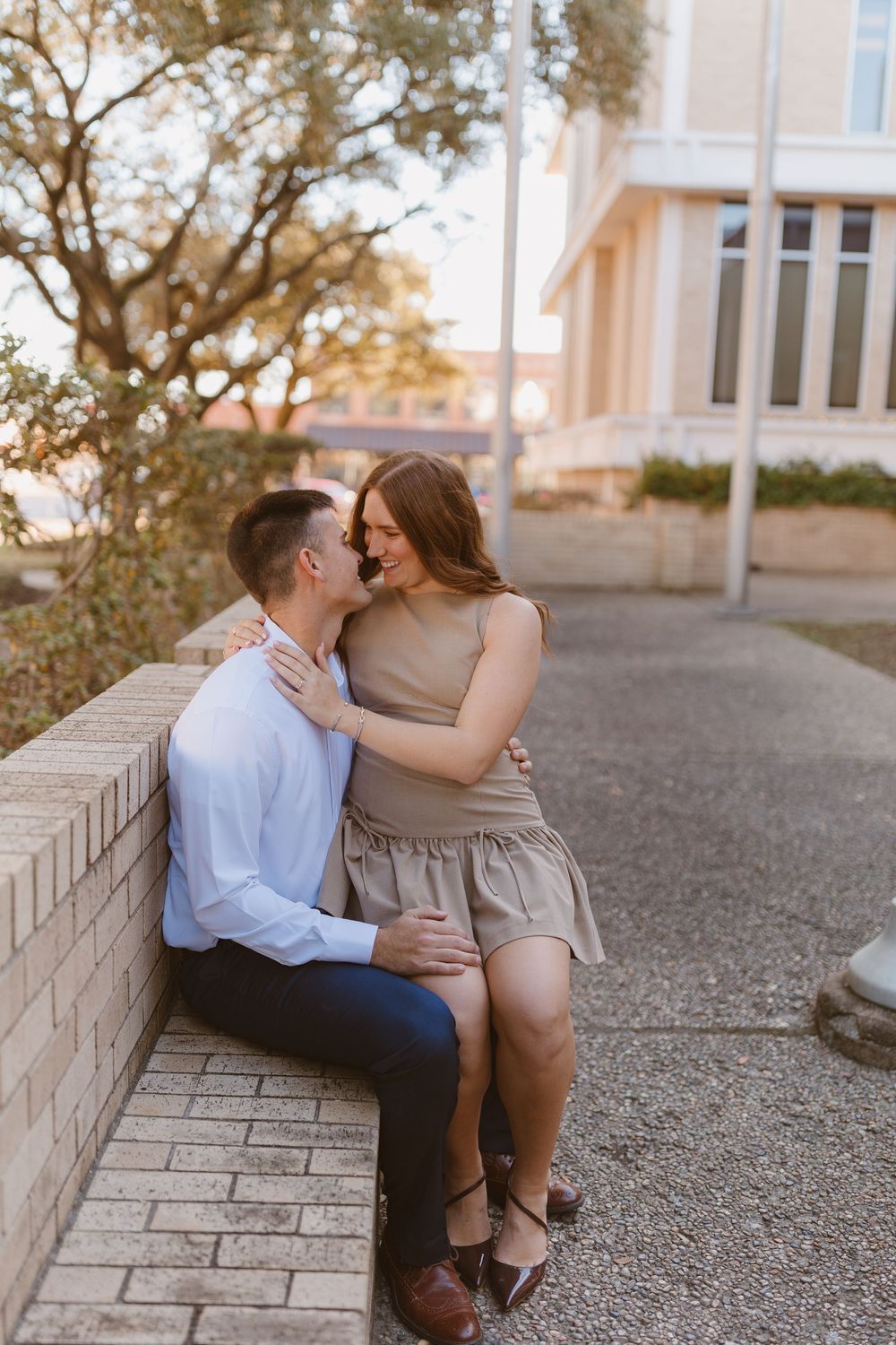 A couple shares an intimate moment sitting together on a brick wall during golden hour at sunset.