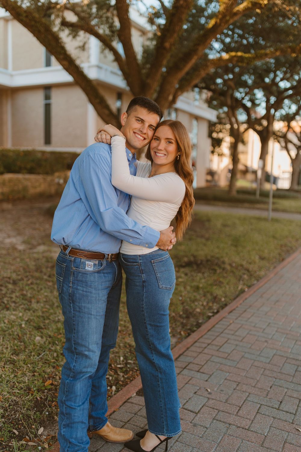 A couple in matching denim and blue outfits embrace while standing on a brick pathway during golden hour.