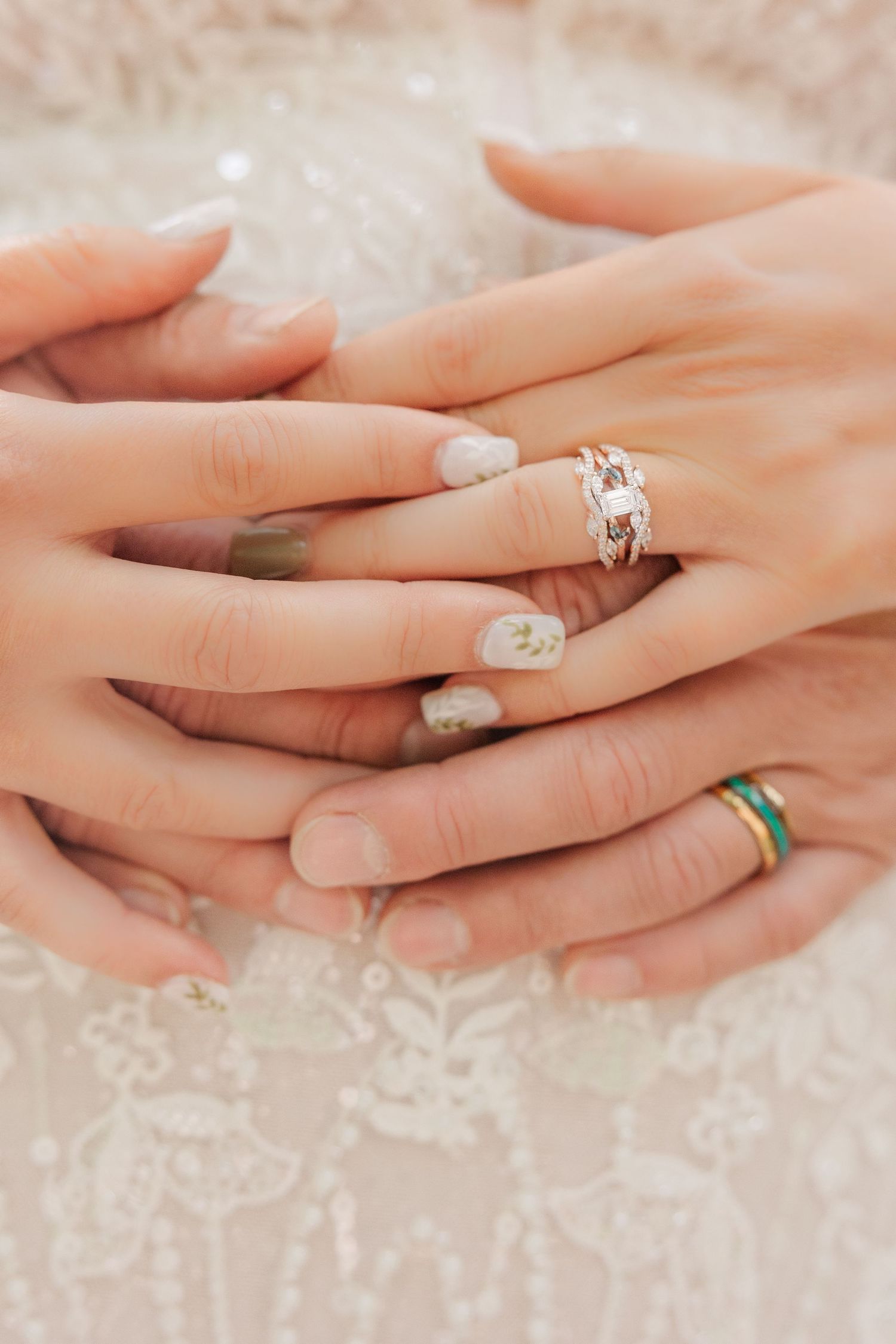 Close-up of hands with elegant engagement ring and decorative nail art against a lacy white background.