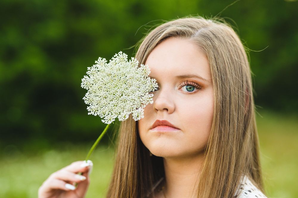 Woman in white holds a delicate Queen Anne's lace wildflower against her face outdoors.