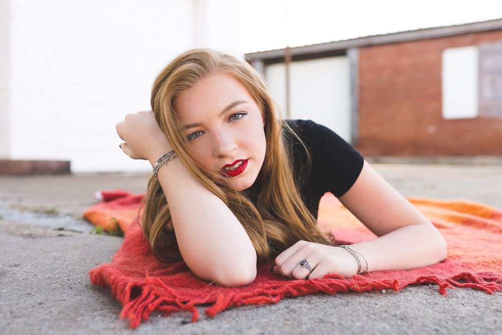 A sequence of portraits shows a person lying on red blanket on concrete ground while posing outdoors.