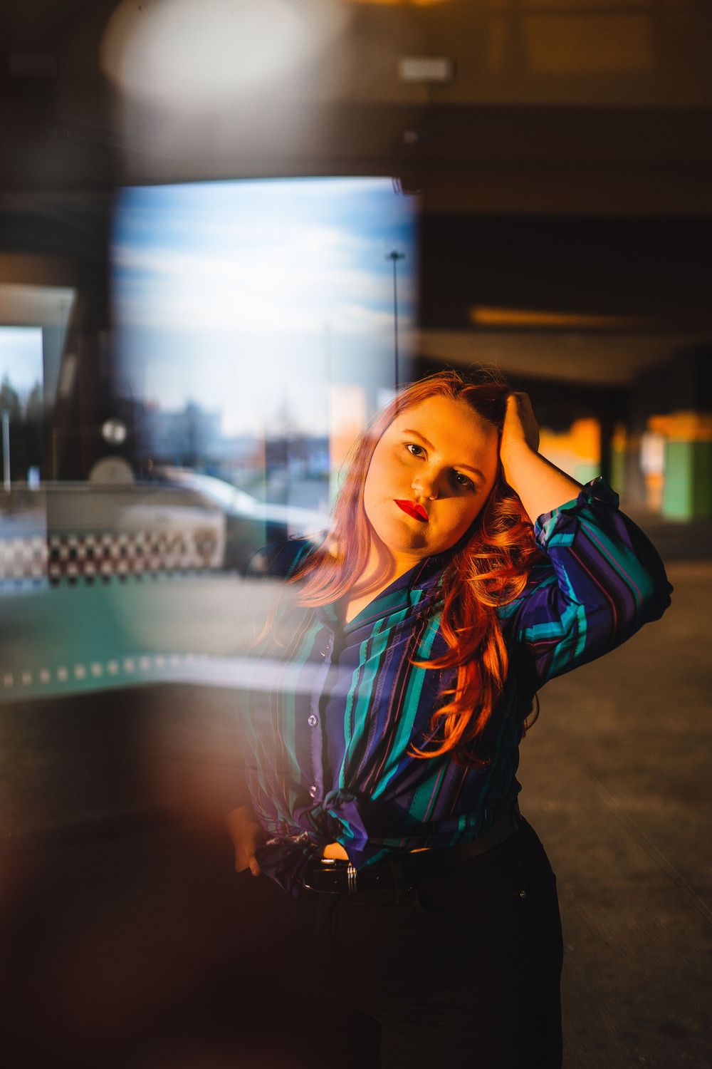 Artistic portrait in a parking garage with dramatic lighting and reflections, featuring a striped retro style shirt.