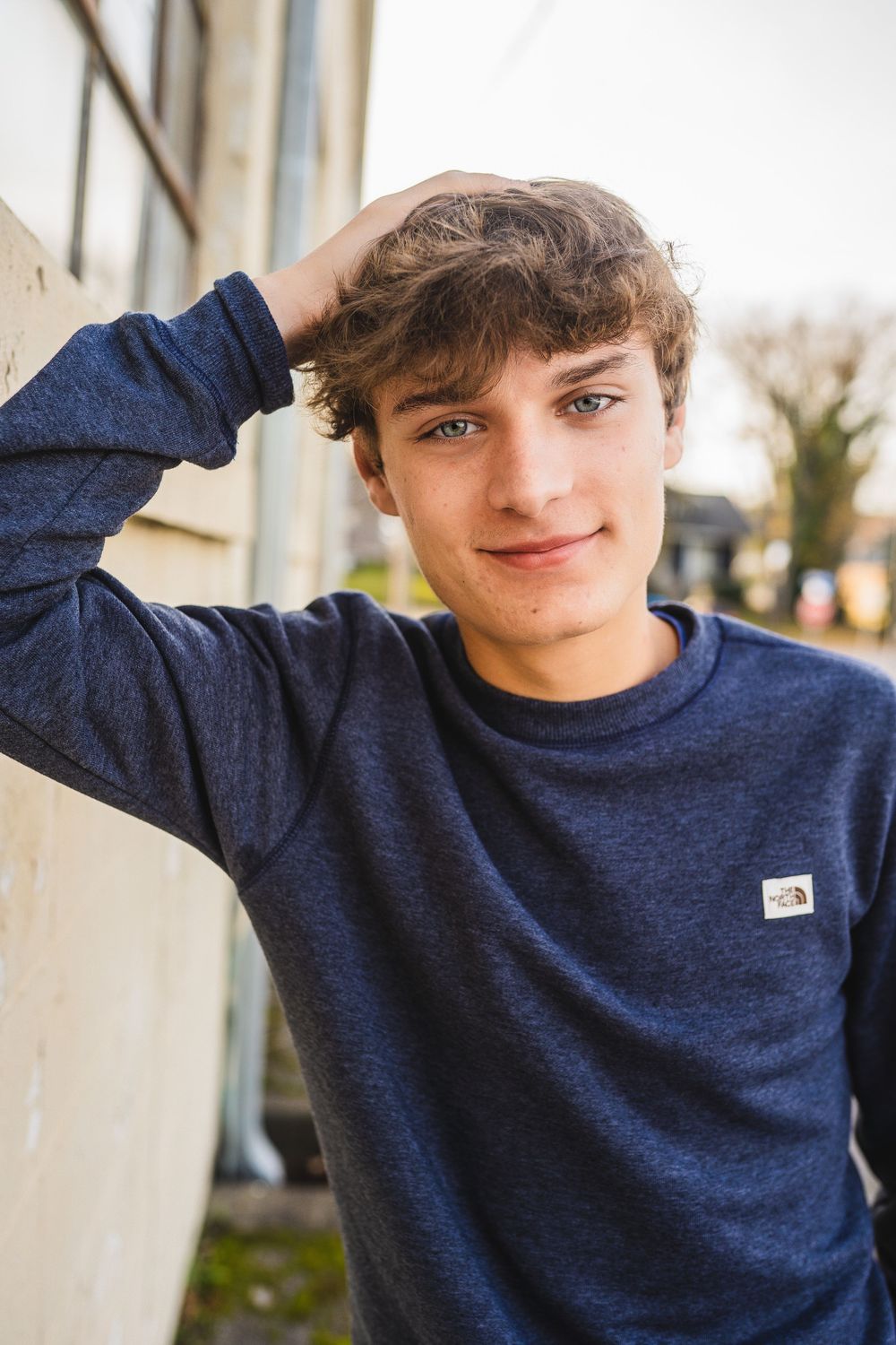 A person wearing a navy blue North Face sweater poses against a light-colored wall in various casual positions.