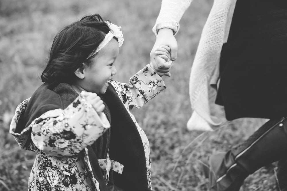 Black and white photo of a small child in floral dress holding an adult's hand while walking outdoors.
