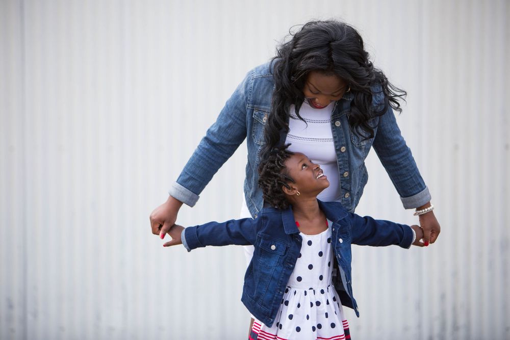 Two people wearing matching denim jackets share a playful moment against a white wall background.