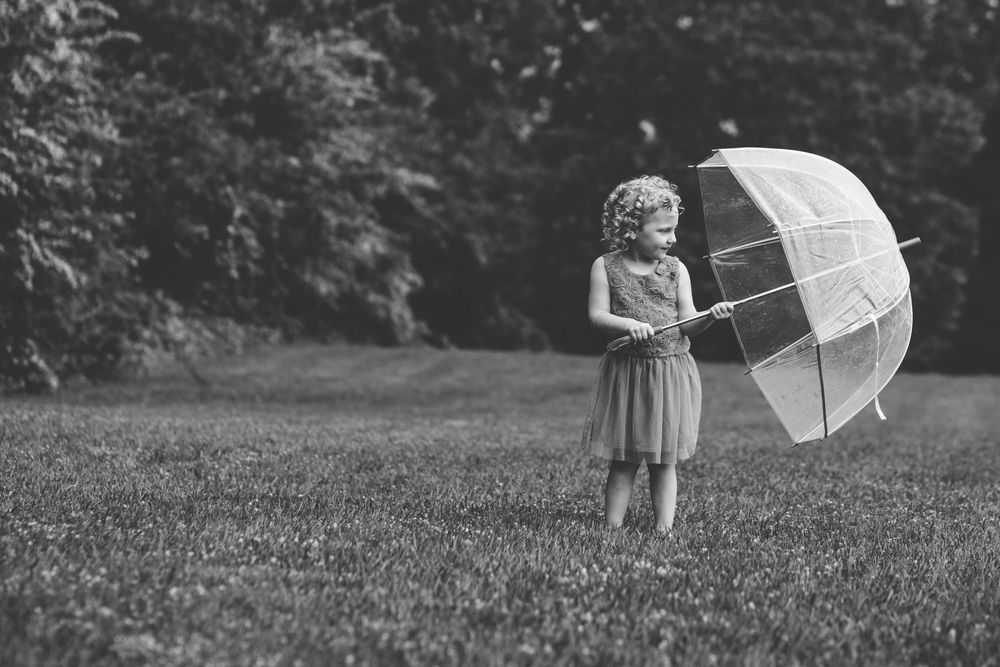 A vintage black and white photo shows a figure in a dress holding a clear bubble umbrella in a grassy field.