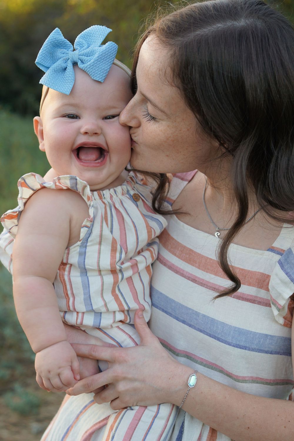 A sequence of loving moments shared between a baby wearing a blue bow and parent in striped clothing outdoors.