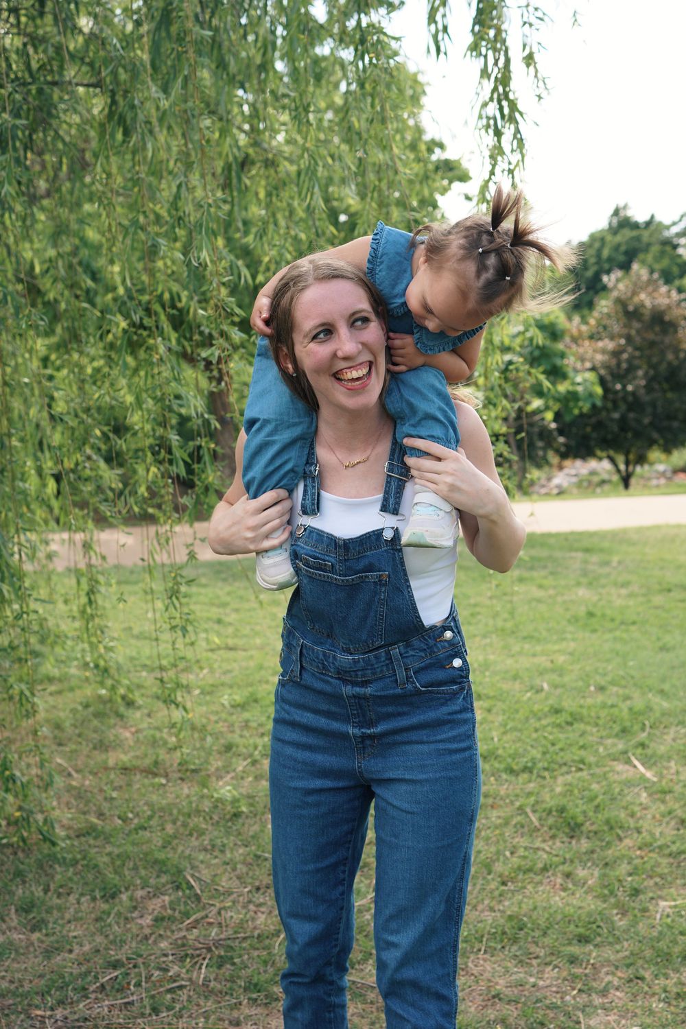 Playful scene outdoors with denim overalls against a backdrop of willow trees and green grass.