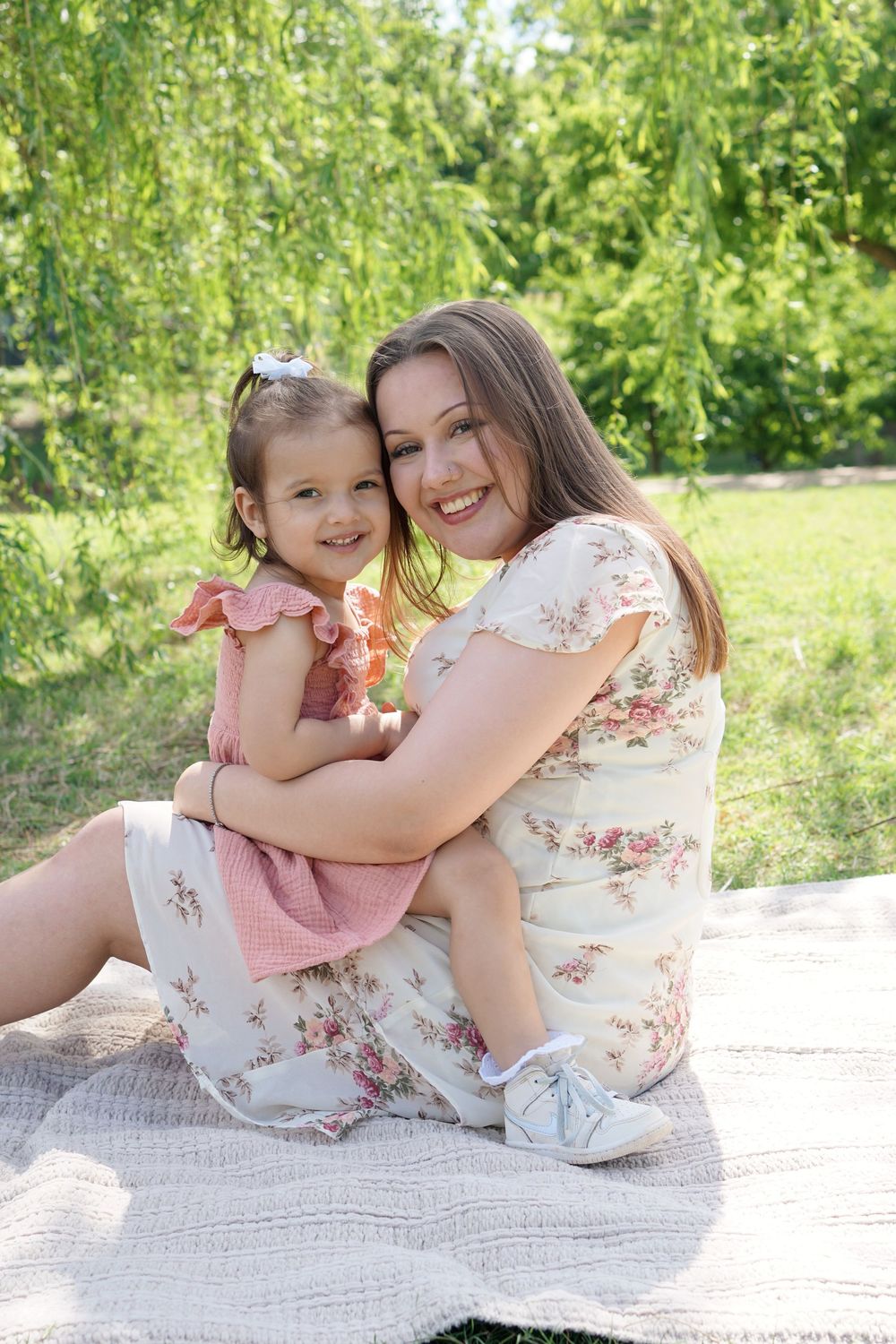 A joyful family moment on a blanket outdoors with floral dresses and smiles on a sunny summer day.