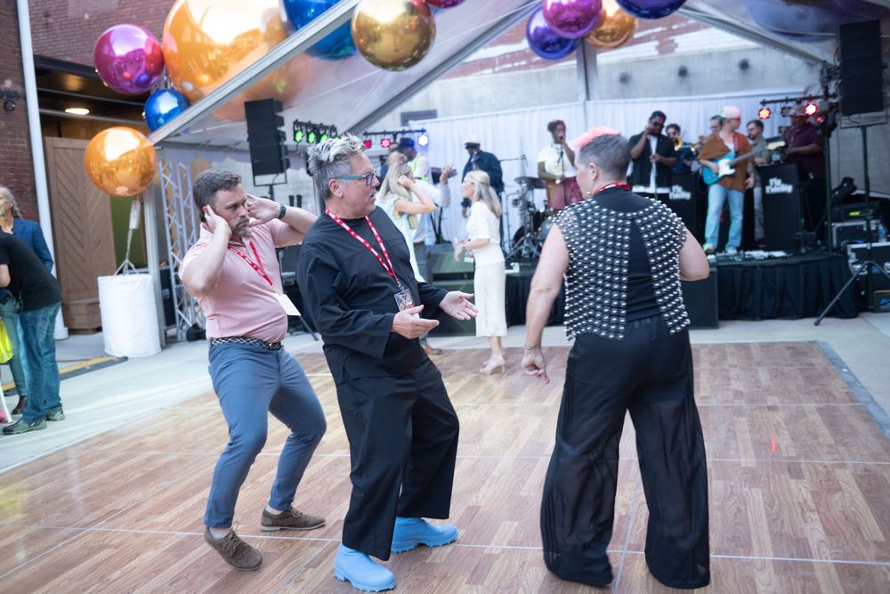 Group of dancers moving together on a wooden dance floor at a social dance event in a bright indoor setting.