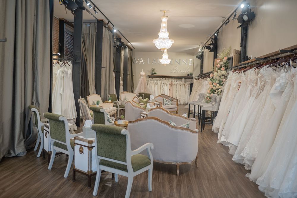 Interior of a bridal boutique with elegant white wedding dresses displayed and vintage-style seating area on wooden floors.