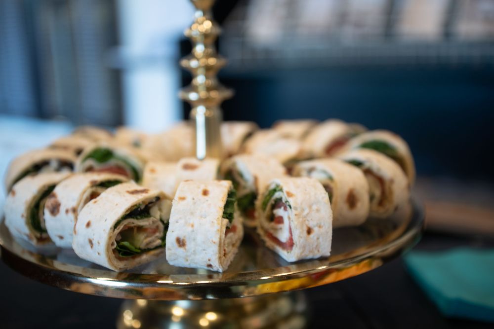 A platter of rolled tortilla pinwheel sandwiches filled with meat and vegetables arranged on a gold serving stand.