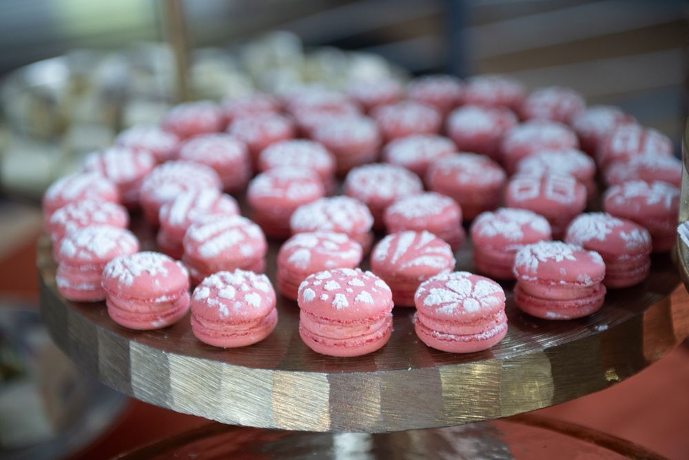 Pink macarons with sparkly sugar decorations arranged in a circular pattern on a wooden serving platter.