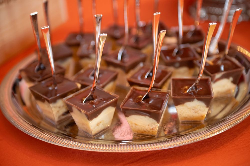 Bite-sized chocolate dessert squares with toothpicks served on a silver platter against an orange background.