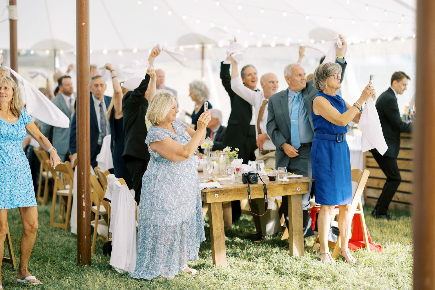 Wedding guests celebrate under a white tent, raising their arms joyfully during an outdoor reception celebration.