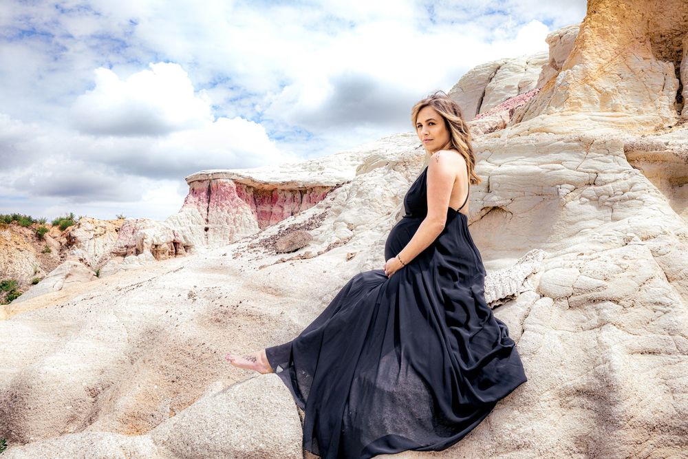 A person in a flowing black dress poses dramatically against white rock formations in a desert landscape.