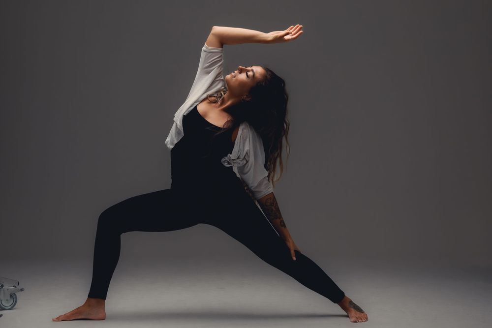 Contemporary dancer performs expressive movement sequence in dark studio with dramatic lighting and flowing movement.