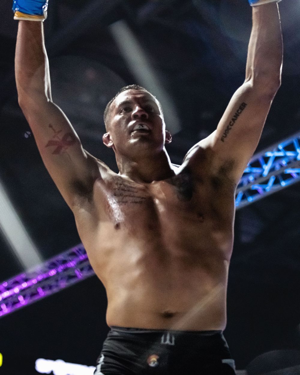 Athletic performer celebrates victory with arms raised in an arena setting with colorful lighting effects in background.