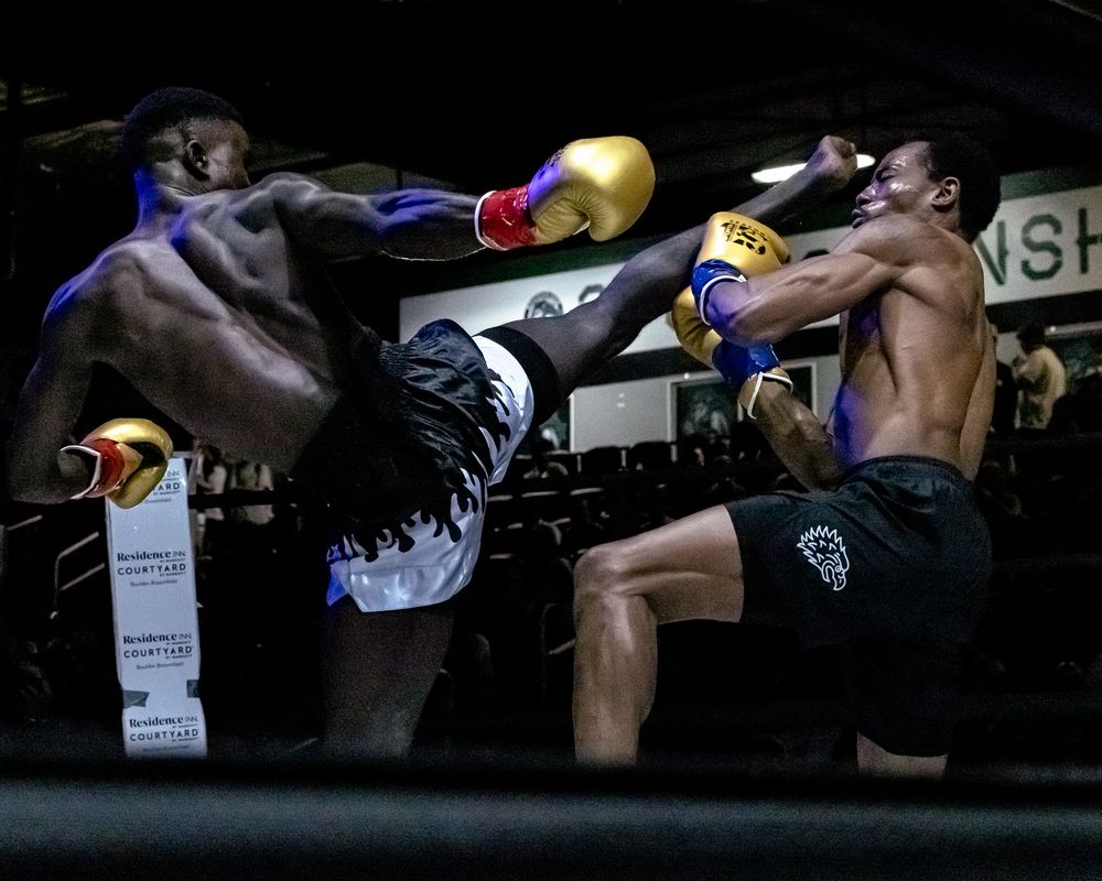 Two fighters exchange powerful kicks during an intense Muay Thai match in a boxing ring.