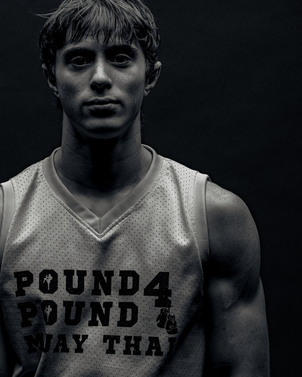 Black and white portrait of an athlete wearing a Pound 4 Pound Muay Thai tank top against dark background.